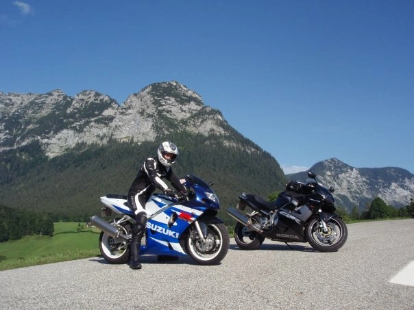 Two sport motorcycles, a Suzuki GSX-R and a Honda CBR, parked on an Alpine road with dramatic limestone peaks in the background, captured during a European motorcycle tour with Freek Jurg.